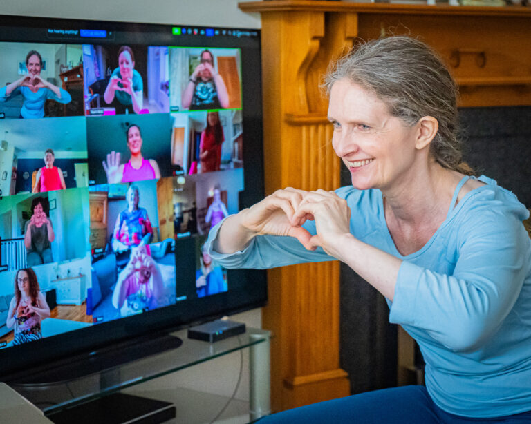 Kerry from mobilates holding her hands up in a heart shape to members on an online exercise class