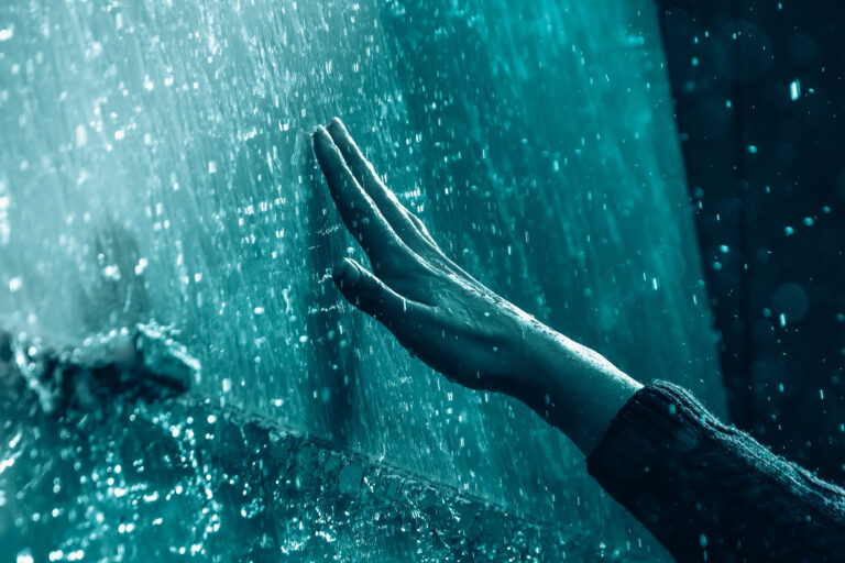 Person reaching their hand out to touch a wall of ice.