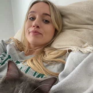 Martha is lying on her side in bed with her grey and white fluffy cat. She looks sad and unwell.