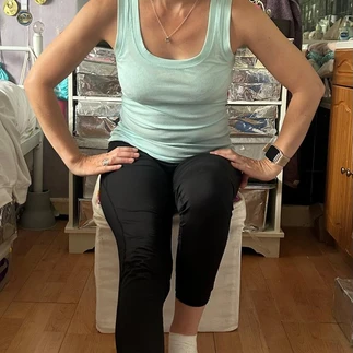 Suzanne demonstrating a hamstring stretch whilst seated. She has one leg straight in front and is wearing a strappy turquoise top and black leggings.