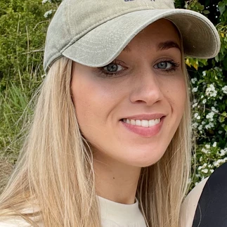 Martha wearing a grey cap smiling. She has long blond hair and is wearing a white t shirt.at the camera. S