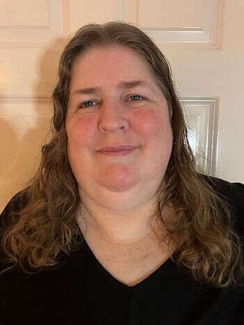 A picture of Debbie smiling at the camera wearing a black v neck top with long brown wavy hair.
