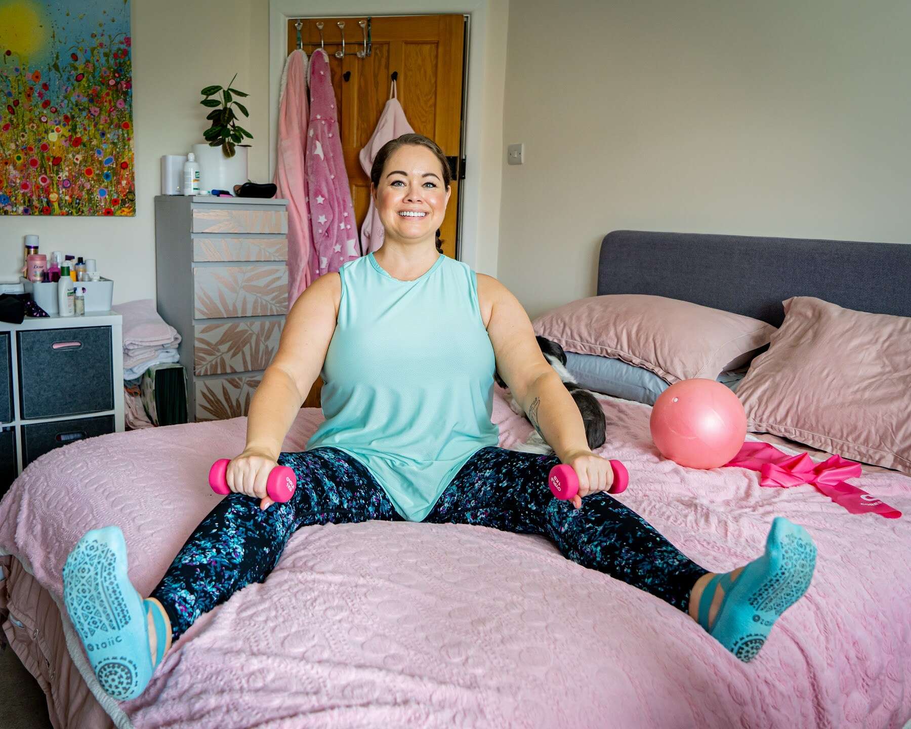 Mobilates member exercising with hand weights while seated on a bed.